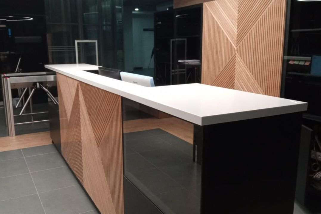 Белая столешница из акрилового камня на стойке с черным низом и деревянными панелями с геометрией, современный интерьер офиса или бизнес-центра.