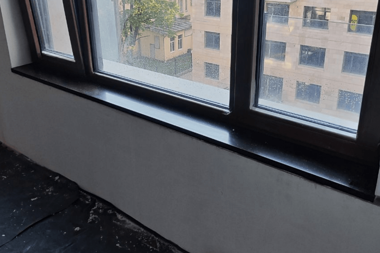 Чёрный подоконник из акрилового камня с глянцевой поверхностью, установлен на этапе ремонта в жилом доме с панорамными окнами